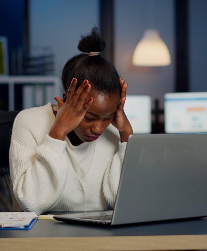 Stressed african businesswoman suffering from headache at work doing overtime late night. Exhausted tensed worker coping with migraine, emotional stress concept feeling pain working at laptop